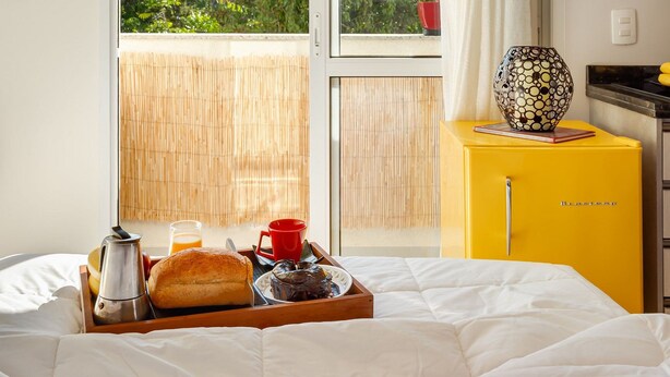 A room with a bed, breakfast tray, yellow cabinet, and a window with a view of greenery. - Studio c/ churrasq 650m da Torre Panorâmica RME047 (Curitiba)