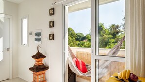A room with a large window, a hammock, a traditional lantern, and a fruit basket on a yellow table. - Studio c/ churrasq 650m da Torre Panorâmica RME047 (Curitiba)