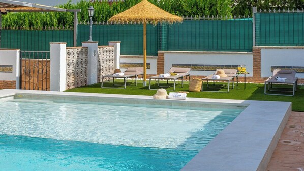 A swimming pool with lounge chairs and a thatched umbrella.