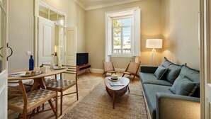 A living room with a sofa, chairs, a coffee table, a television, and a window with a lamp.