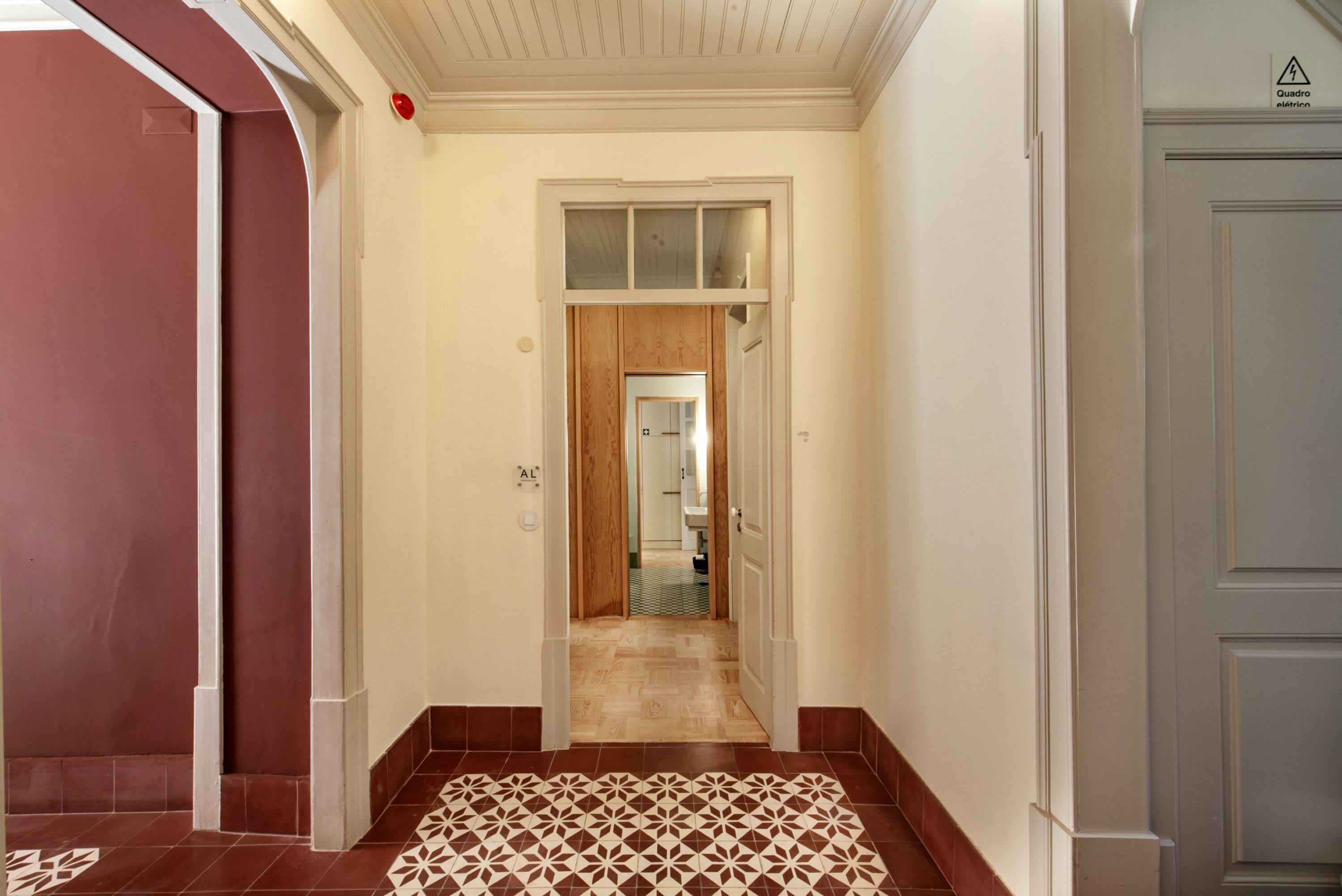 Un pasillo con piso estampado, una puerta de madera y vista al baño.