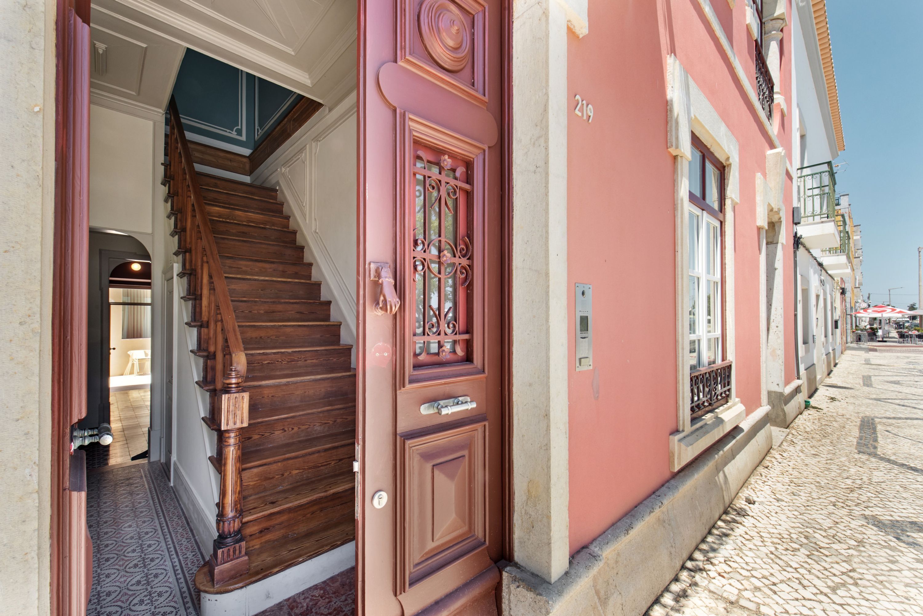 A staircase leading to a door with a decorative metal grille, a cobblestone street, and a building with a number '219' on the facade.