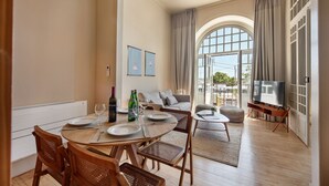 A dining area with a round table, chairs, and a TV in the background. - PG - 1D - T2 Superior - Palacete do Guadiana (Vila Real Santo Antonio)