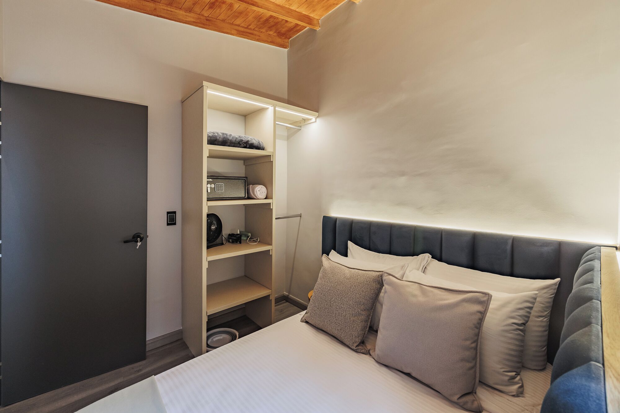 Un dormitorio con una cama, un armario y una estantería empotrada con varios objetos.
