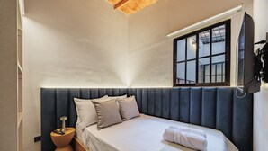 Un dormitorio con cama, mesita de noche, ventana y televisor de pared.