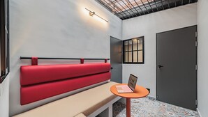 Una habitación moderna con un banco rojo, una pequeña mesa con una computadora portátil, una puerta y baldosas de suelo con diseños.