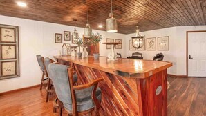A rustic kitchen with a wooden island, pendant lights, and framed botanical prints on the walls.