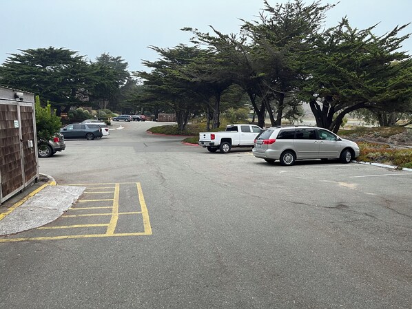 A parking lot with several cars, including a white pickup truck and a silver SUV, parked along a road lined with trees.