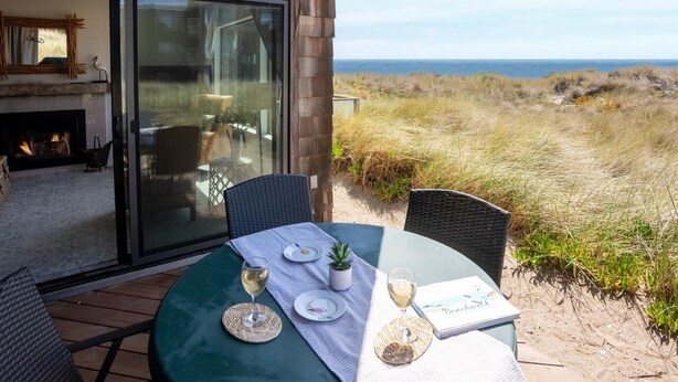 Ein Essbereich im Freien mit Blick auf Strand und Meer, mit einem Tisch, Geschirr, Gläsern und einer Speisekarte.