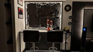 A modern kitchen with a stone backsplash, two bar stools, and a built-in wine rack. - Escape Studio (Kingston)