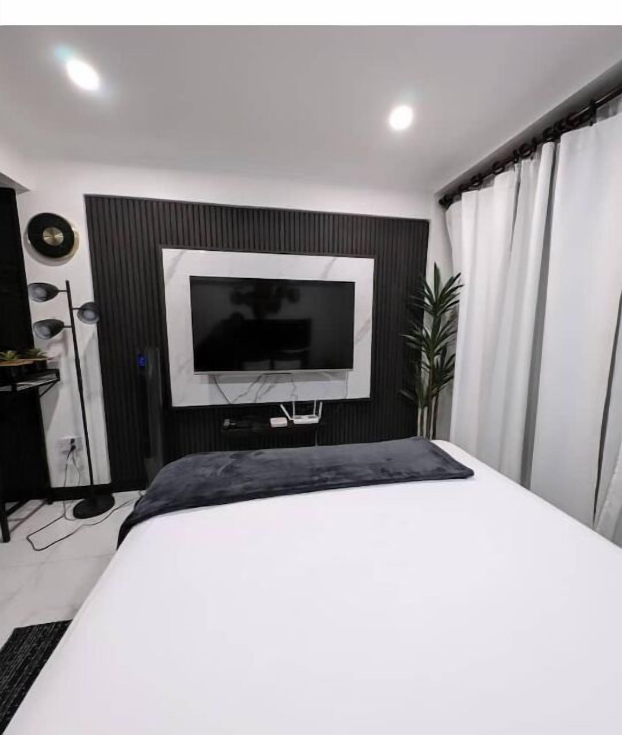 Quarto moderno com uma cama grande, televisão montada e um vaso com planta.