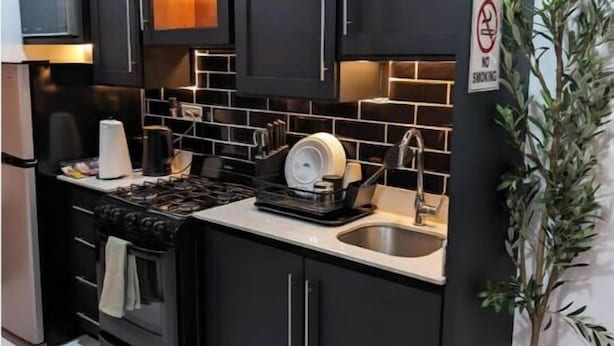 A modern kitchen with dark cabinetry, a gas stove, and a sink. - Escape Studio (Kingston)