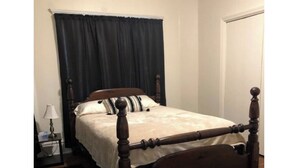 Ein Einzelbett mit Holzrahmen und weißer Matratze in einem Zimmer mit Holzboden und einem dunklen Vorhang.