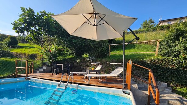 Ein Schwimmbecken mit Holzterrasse, Liegestühlen und Sonnenschirm.