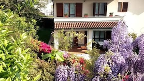 Ein zweistöckiges Haus mit Ziegeldach, einem Balkon und einem Garten mit violetten Blumen.