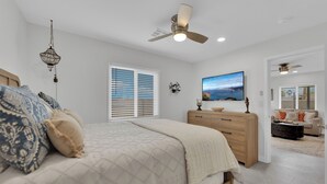 A bedroom with a bed, a dresser, a ceiling fan, and a painting on the wall.