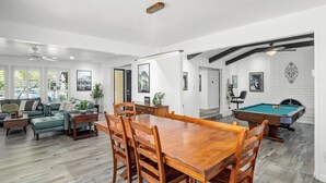 Een ruime woonkamer met een houten eettafel, zithoek, een pooltafel en een open haard.
