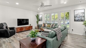 Een moderne woonkamer met een groene bank, een houten salontafel, een zwarte fauteuil en een televisie op een houten kast.