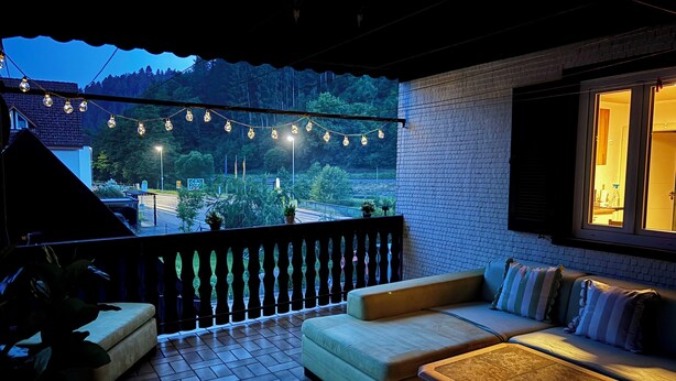 Un balcon avec un canapé, une table et des guirlandes lumineuses.