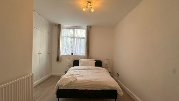 Ein Schlafzimmer mit Bett, Fenster, Heizkörper und Kleiderschrank.
