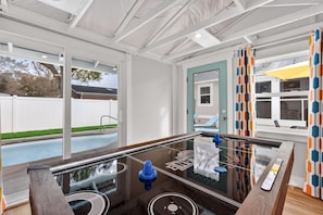 A room with a glass-top pool table, large windows, and a view of a backyard.