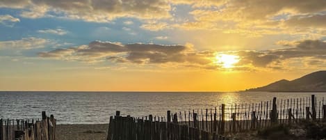 Un sendero de playa con valla de madera que lleva al mar, bajo un cielo al atardecer.