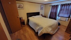 A bedroom with a bed, a nightstand, a small table, a window with curtains, and a radiator. - Remodeled Cottage 4 at the King Creek Lodge and Marina (Benton)
