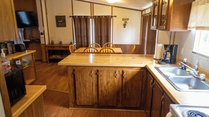 A compact kitchen with wooden cabinets, a central island, a dining table with chairs, a microwave, a coffee maker, and a stove. - Remodeled Cottage 4 at the King Creek Lodge and Marina (Benton)