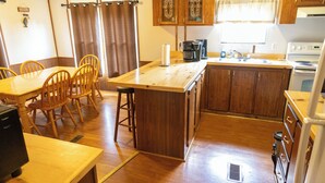 A compact kitchen with wooden cabinets, a central island, and a dining area with chairs. - Remodeled Cottage 4 at the King Creek Lodge and Marina (Benton)