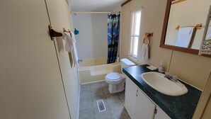 A bathroom with a bathtub, toilet, sink, and a shower curtain. - Remodeled Cottage 4 at the King Creek Lodge and Marina (Benton)