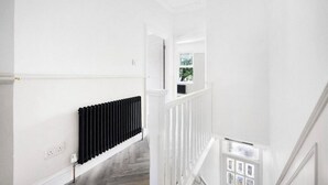 A white interior with a black radiator, white railing, and a window with a view of greenery. - Newly refurbished 2 bedroom apartment in trendy Leyton (London)