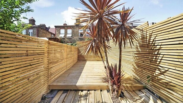A narrow wooden deck with a wooden fence on one side and a brick wall on the other. - Newly refurbished 2 bedroom apartment in trendy Leyton (London)