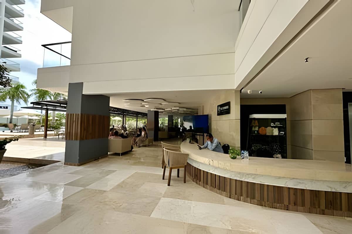 A modern hotel lobby with a reception desk, seating area, and a poolside view.