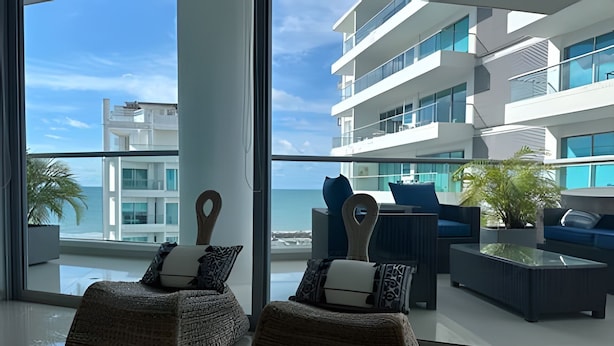 A modern lounge area with wicker furniture and a view of a coastal building. - SONESTA (Cartagena)