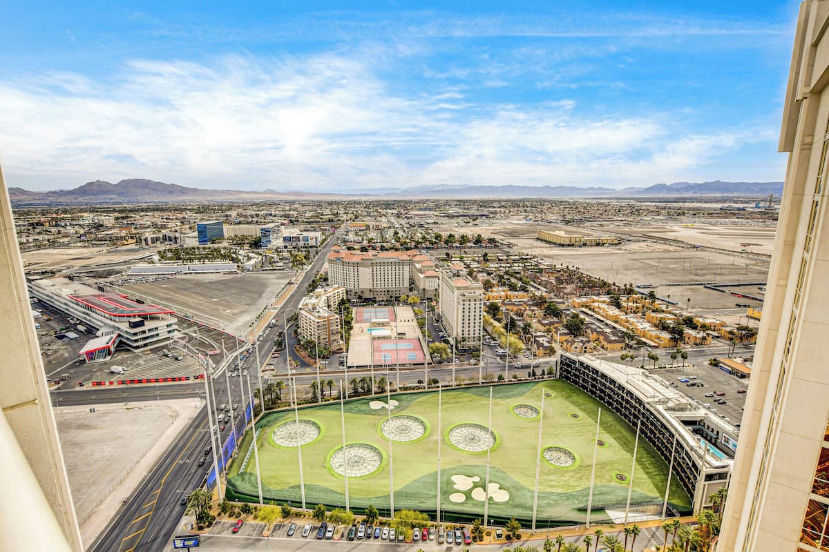 An aerial view of a stadium with a green field, surrounding buildings, and a clear sky.