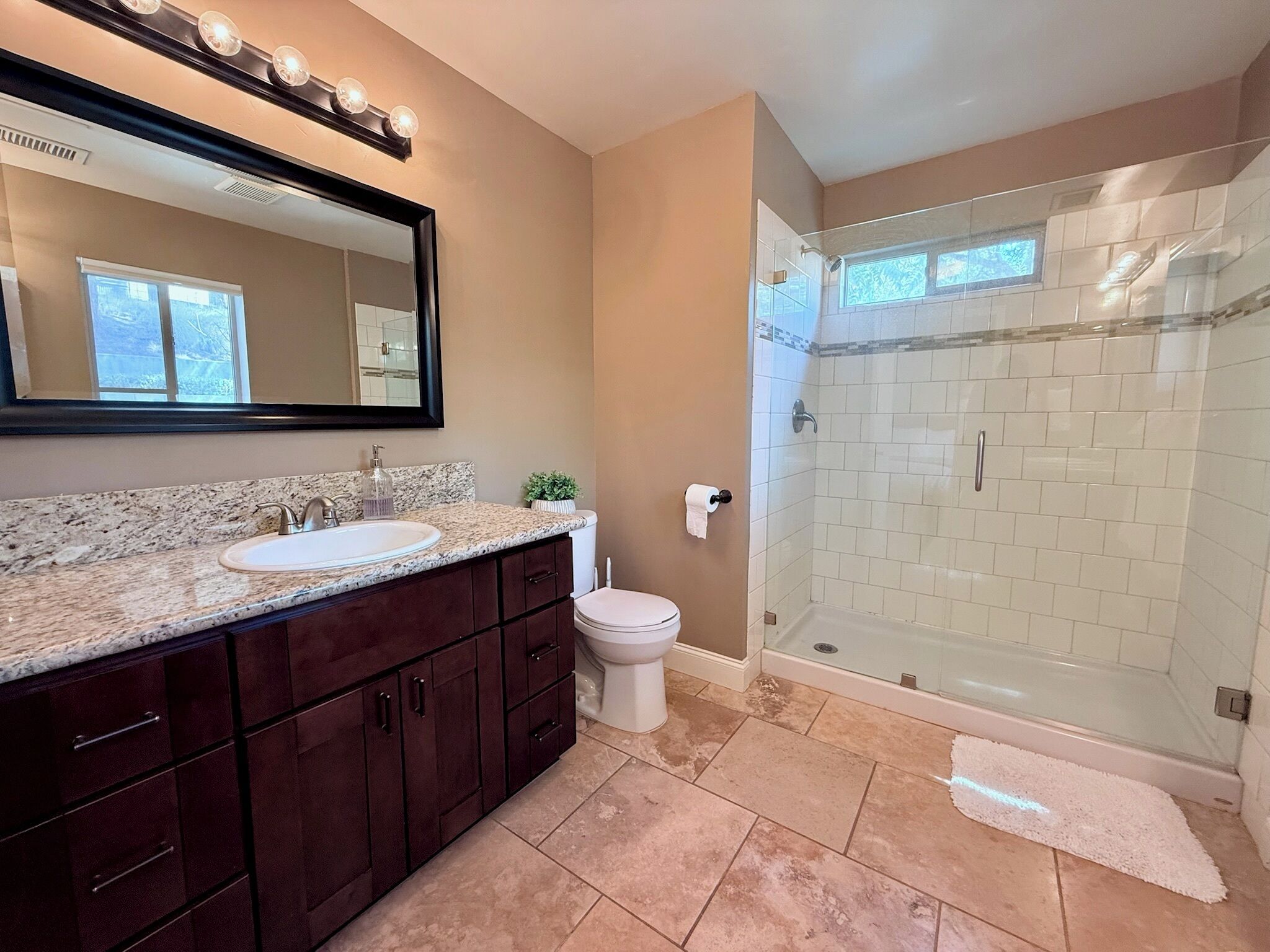 A bathroom with a vanity, sink, mirror, and a walk-in shower.