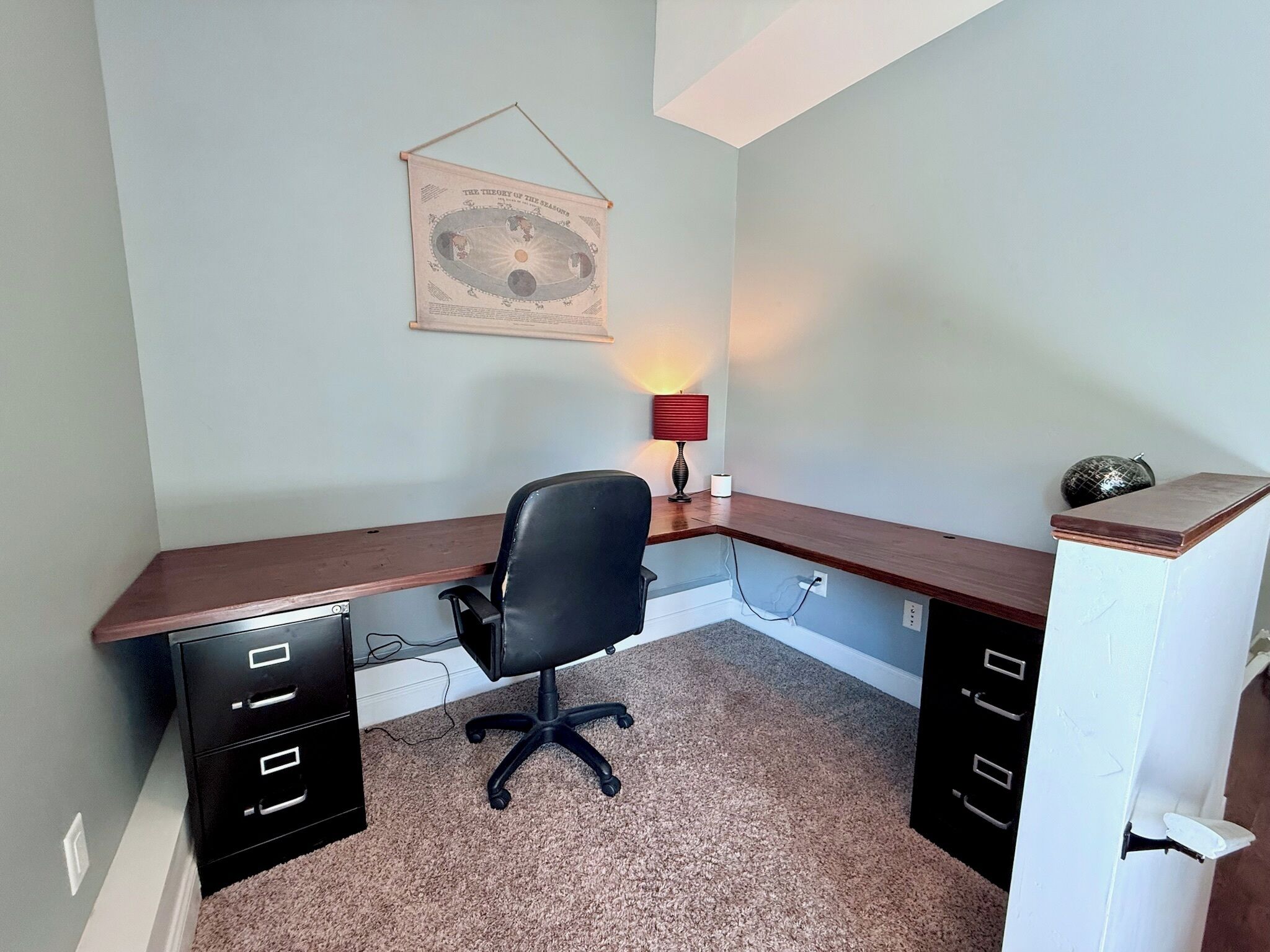 Una oficina en casa con escritorio, silla y lámpara de pared.