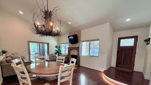 A spacious living room with a round wooden dining table surrounded by chairs, a fireplace, and a television mounted on the wall. - Filbert Reserve (Paso Robles)
