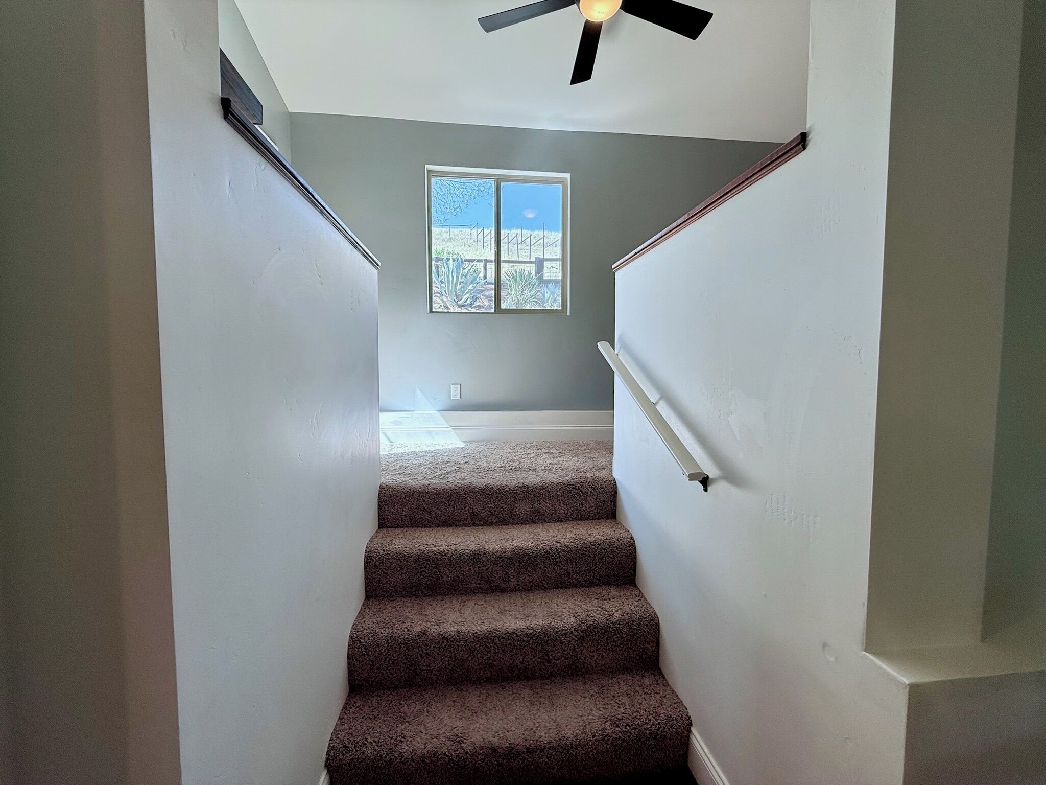 A staircase with carpeted steps leading to a landing with a ceiling fan.