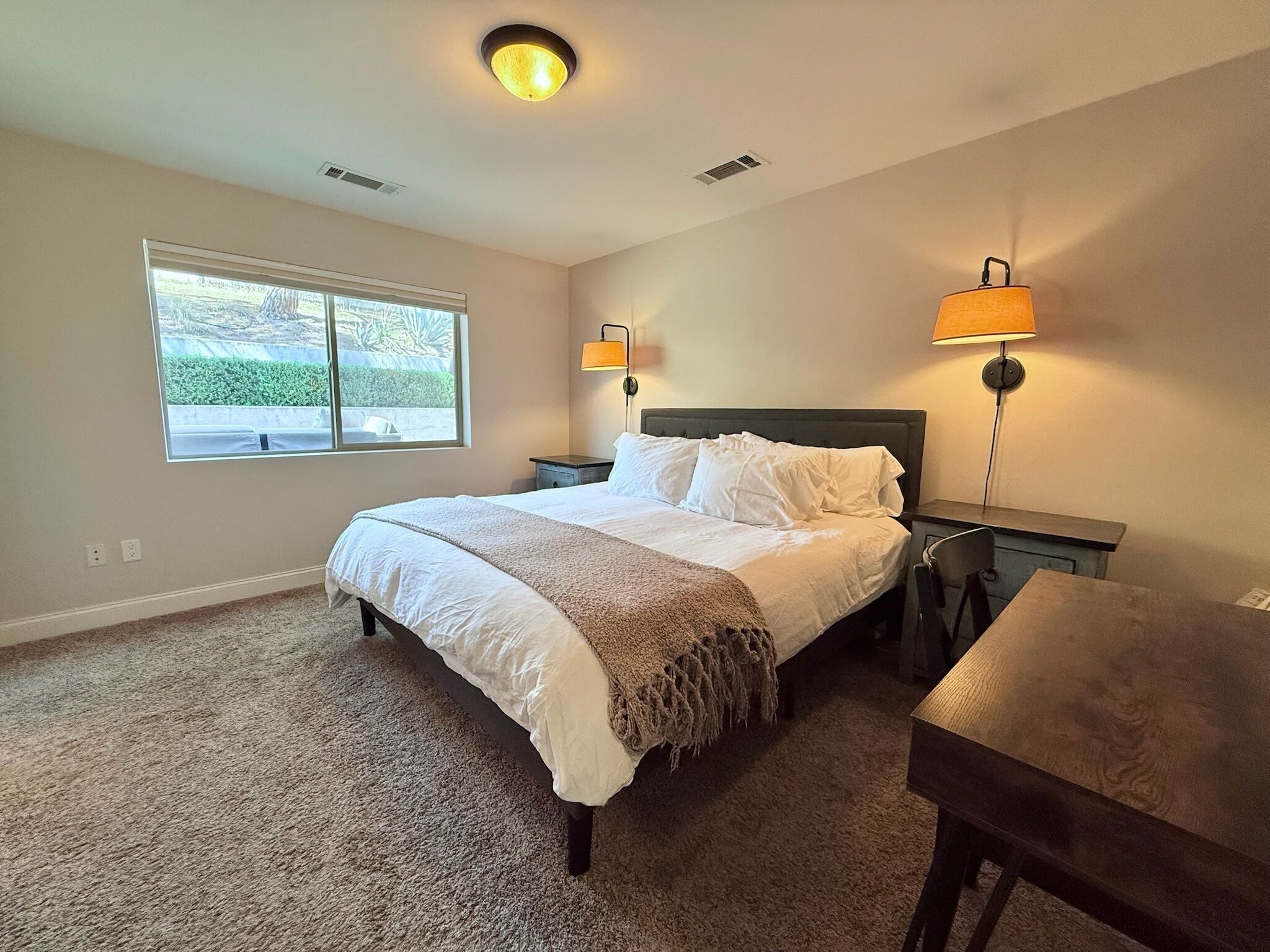 A bedroom with a bed, bedside lamps, a window, and a desk.