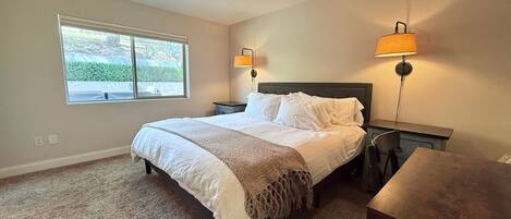 A bedroom with a bed, bedside lamps, a window, and a desk.