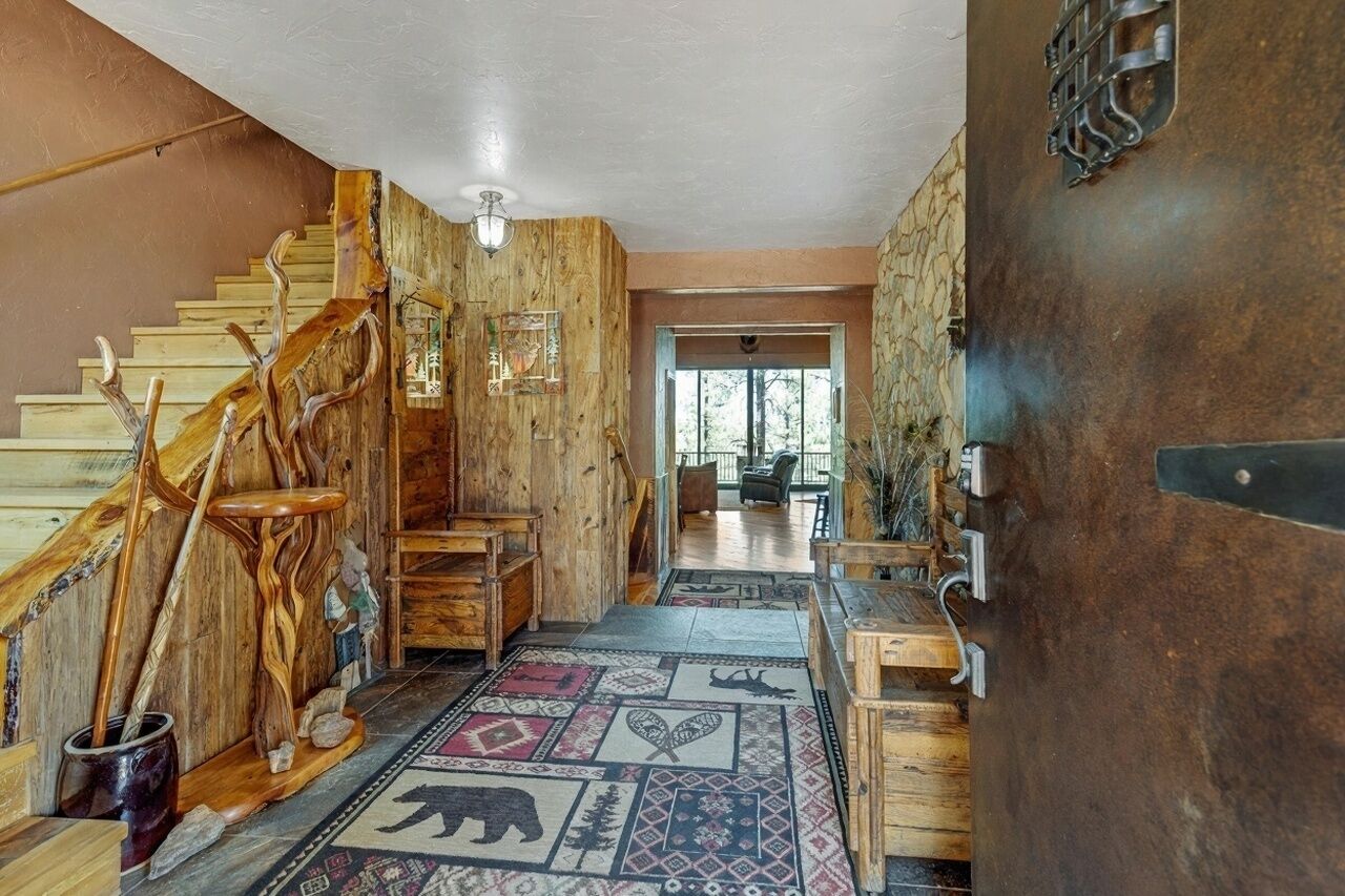 Eine hölzerne Treppe mit rustikalem Design führt zu einem Raum mit einem gemusterten Teppich und einer großen Metalldür.'