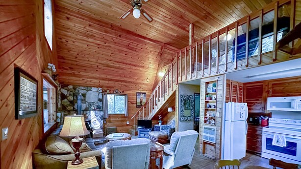A cozy cabin interior with a stone fireplace, wooden walls, a dining area, and a kitchen with modern appliances.