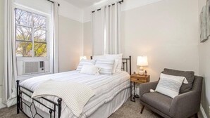 Un dormitorio con una cama, una mesita de noche, una lámpara y un sillón gris.