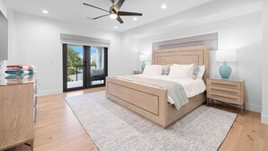A modern bedroom with a large bed, a ceiling fan, a nightstand, and a view through a sliding glass door. - Paradise on Bay Blvd – Heated Pool, Balconies, Elevator & 2 Blocks to Indian Rocks Beach (Indian Rocks Beach)