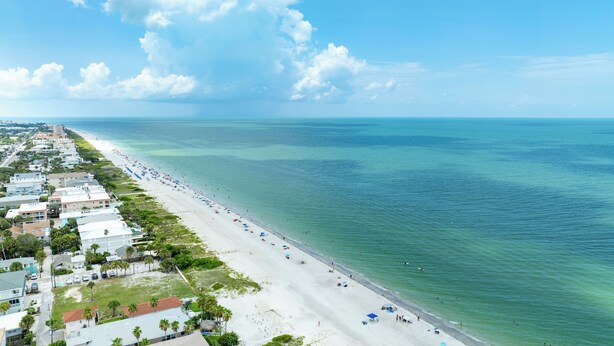 An aerial view of a coastal area with a long beach, clear blue water, and a row of buildings along the shore. - Paradise on Bay Blvd – Heated Pool, Balconies, Elevator & 2 Blocks to Indian Rocks Beach (Indian Rocks Beach)