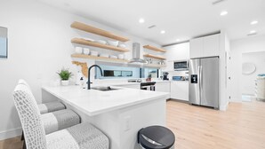 A modern kitchen with white cabinetry, wooden shelves, and a central island. - Paradise on Bay Blvd – Heated Pool, Balconies, Elevator & 2 Blocks to Indian Rocks Beach (Indian Rocks Beach)