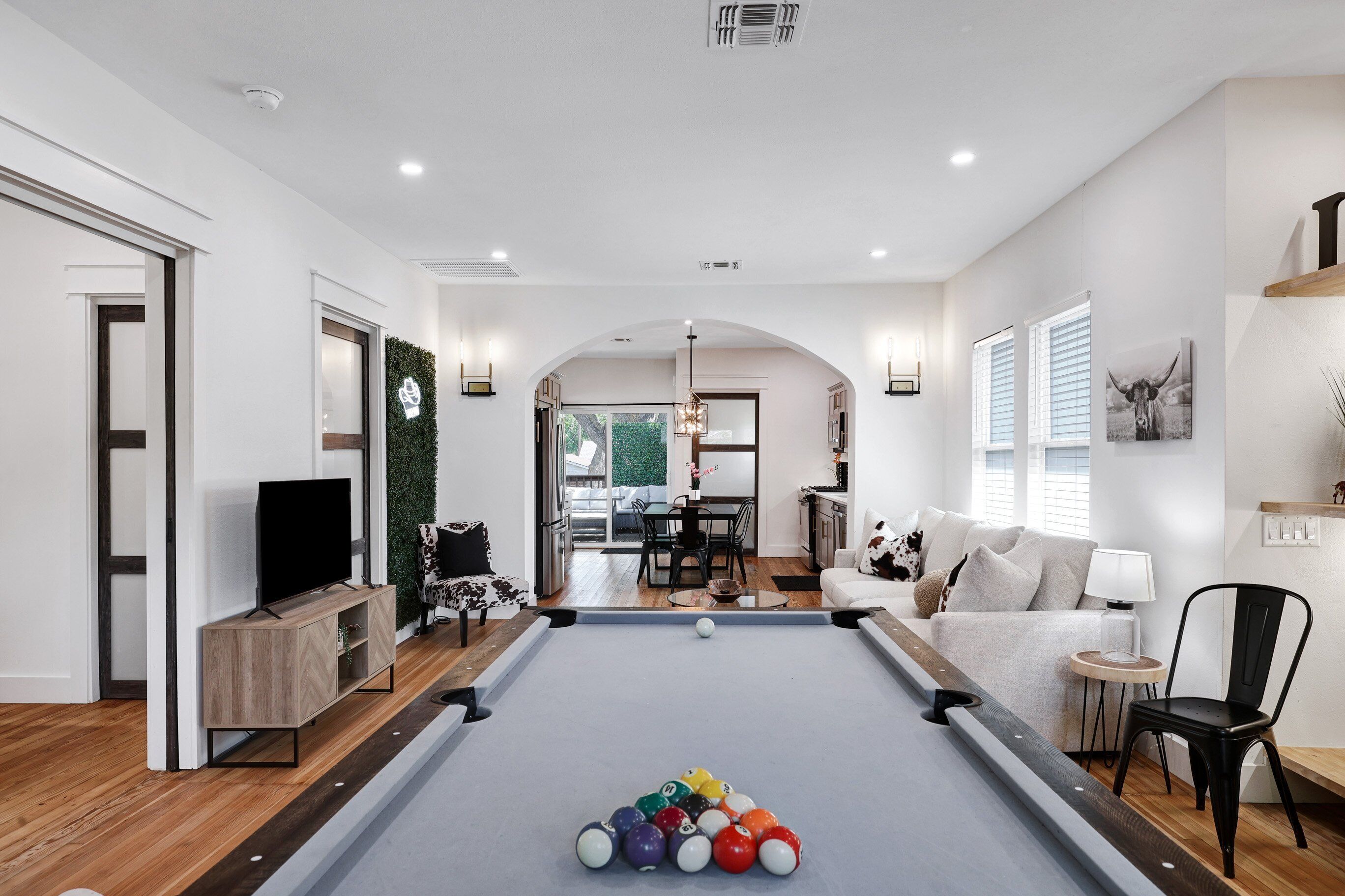 A modern living room with a pool table, a television, and a dining area in the background.