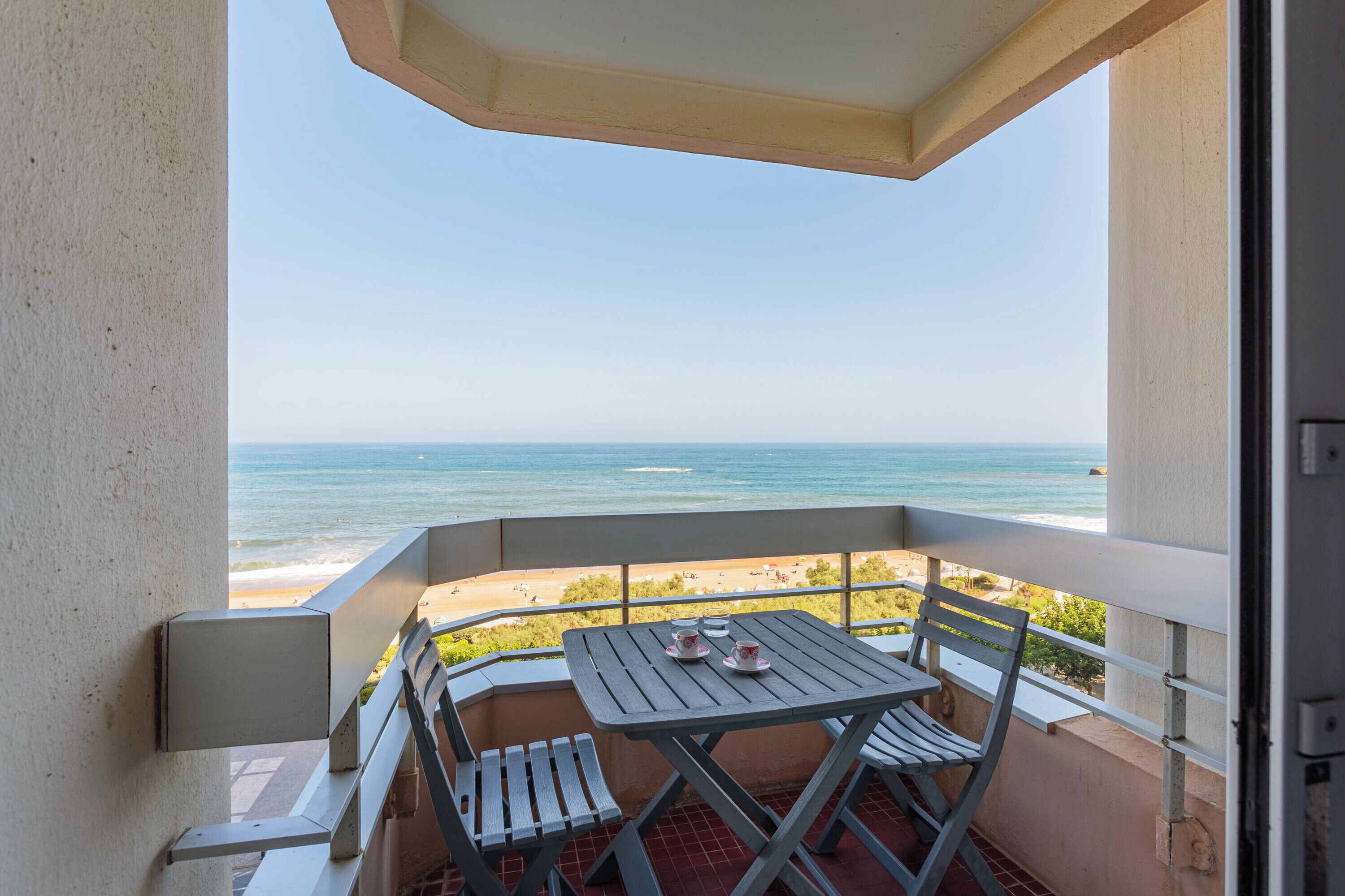 A balcony with a table and chairs overlooking a beach.