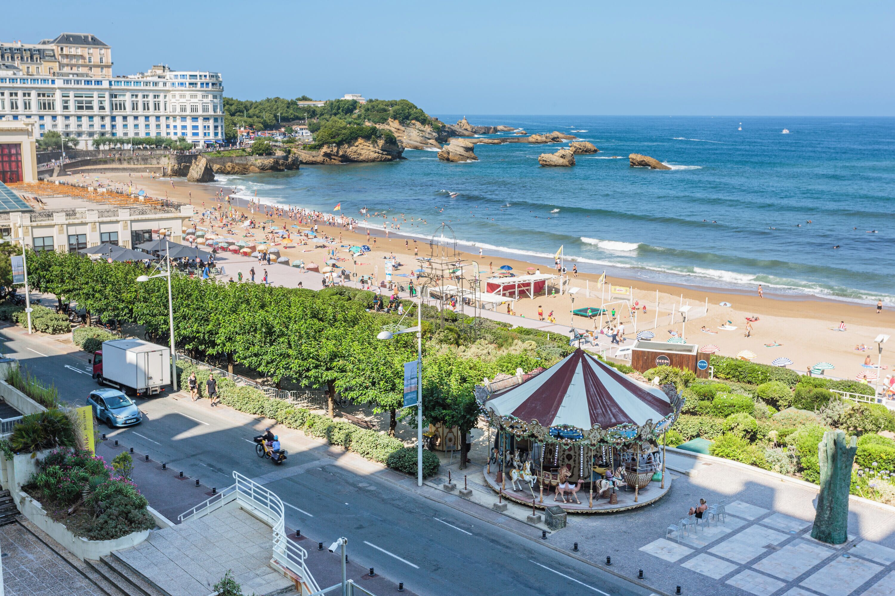Un paisaje urbano costero con una playa, un carrusel y un hotel grande al fondo.